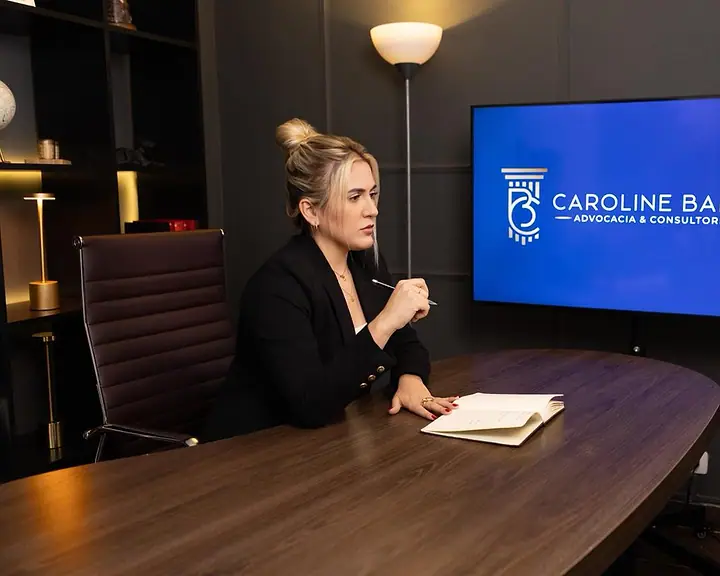 Dra. Caroline Bandeira na sala de reuniões do escritório, com o logo na tela ao fundo