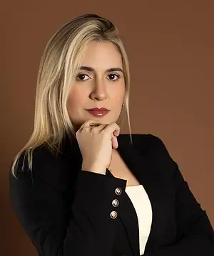 Dra. Caroline Bandeira, de blazer preto, com a mão no queixo, olhando para a câmera