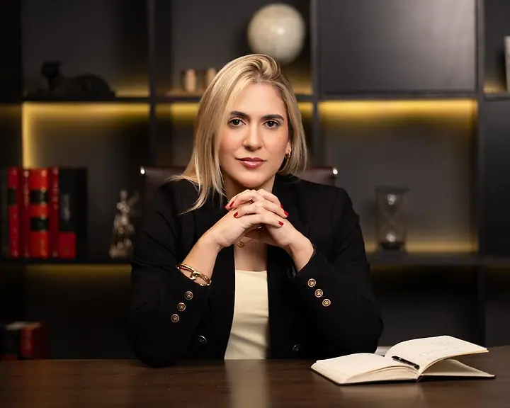 Dra. Caroline Bandeira à mesa do escritório, com as mãos juntas e um caderno aberto