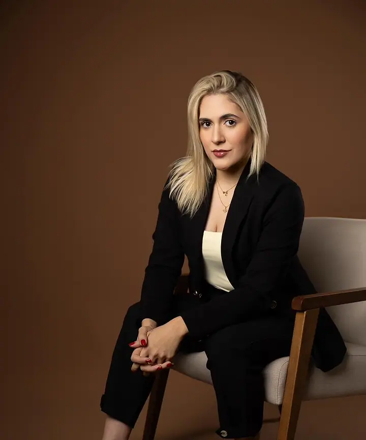 Dra. Caroline Bandeira, de terno preto, sentada em uma cadeira, olhando para a câmera